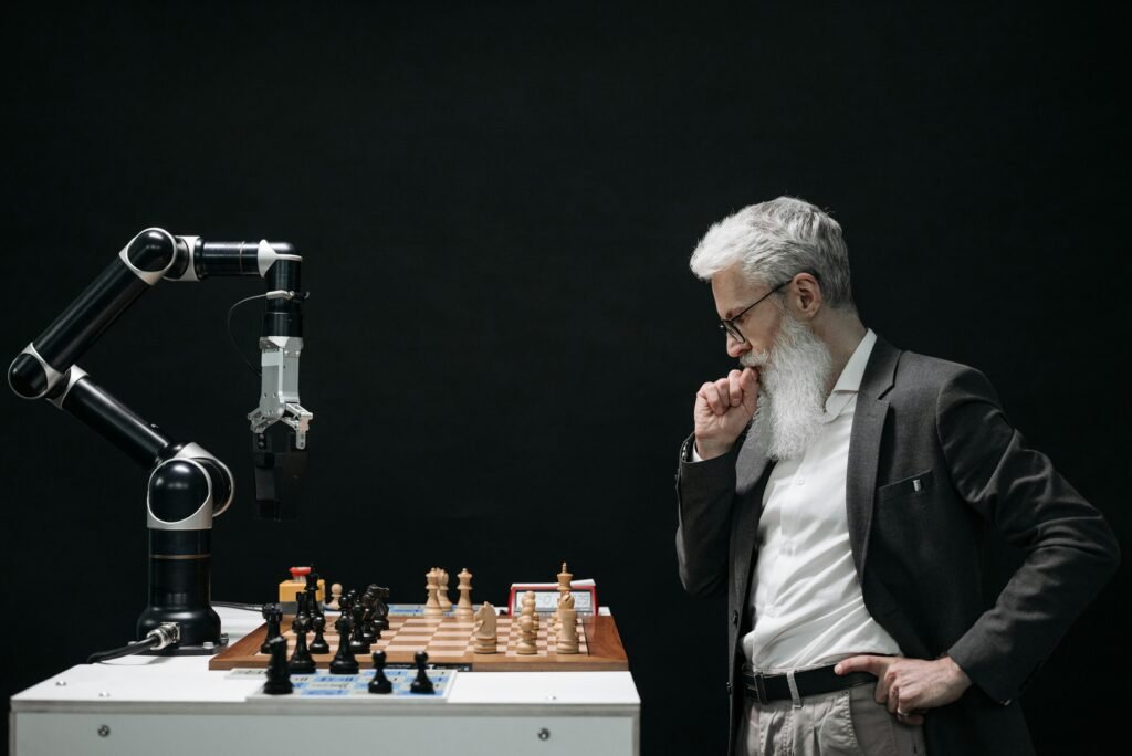 blog An elderly scientist contemplates a chess move against a robotic arm on a chessboard.
