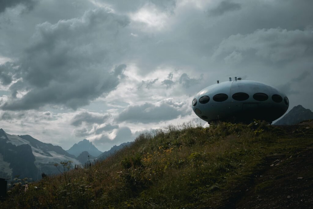 blog Unique UFO-like structure on a grassy hill with a cloudy mountain backdrop.